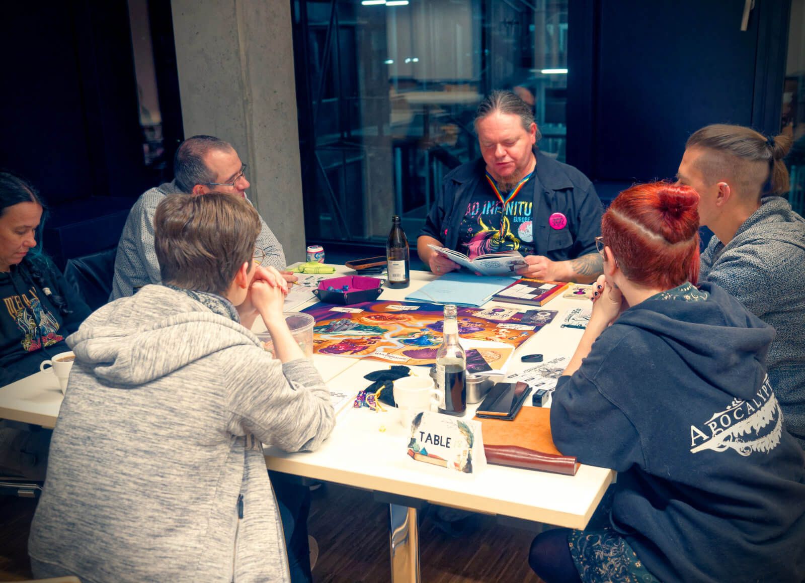 Frank GMing at a table with five players, two men, three women, lost in the books and story.