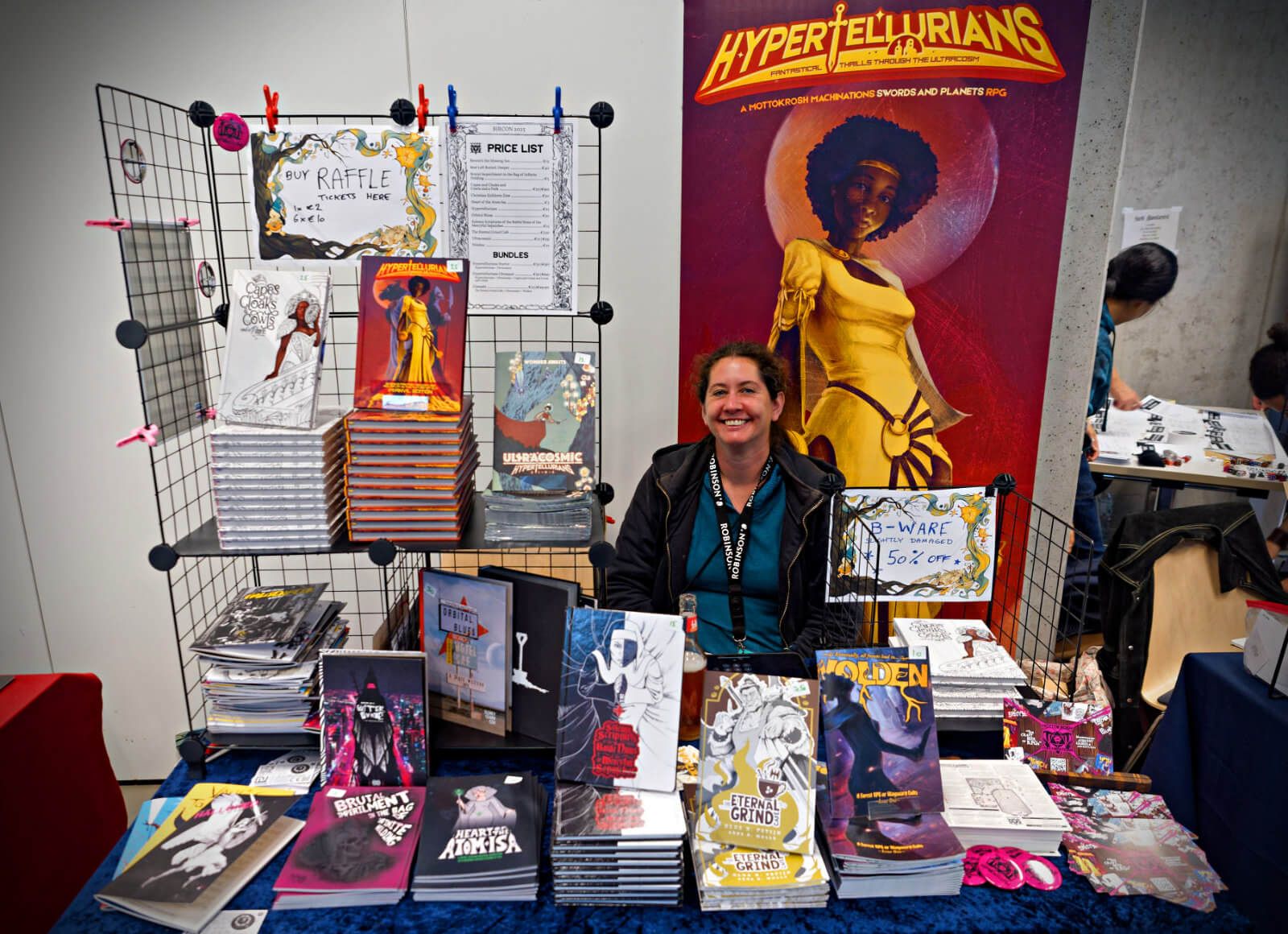 The Mottokrosh Machinations stall, with many books on display, and Karen smiling at the back.